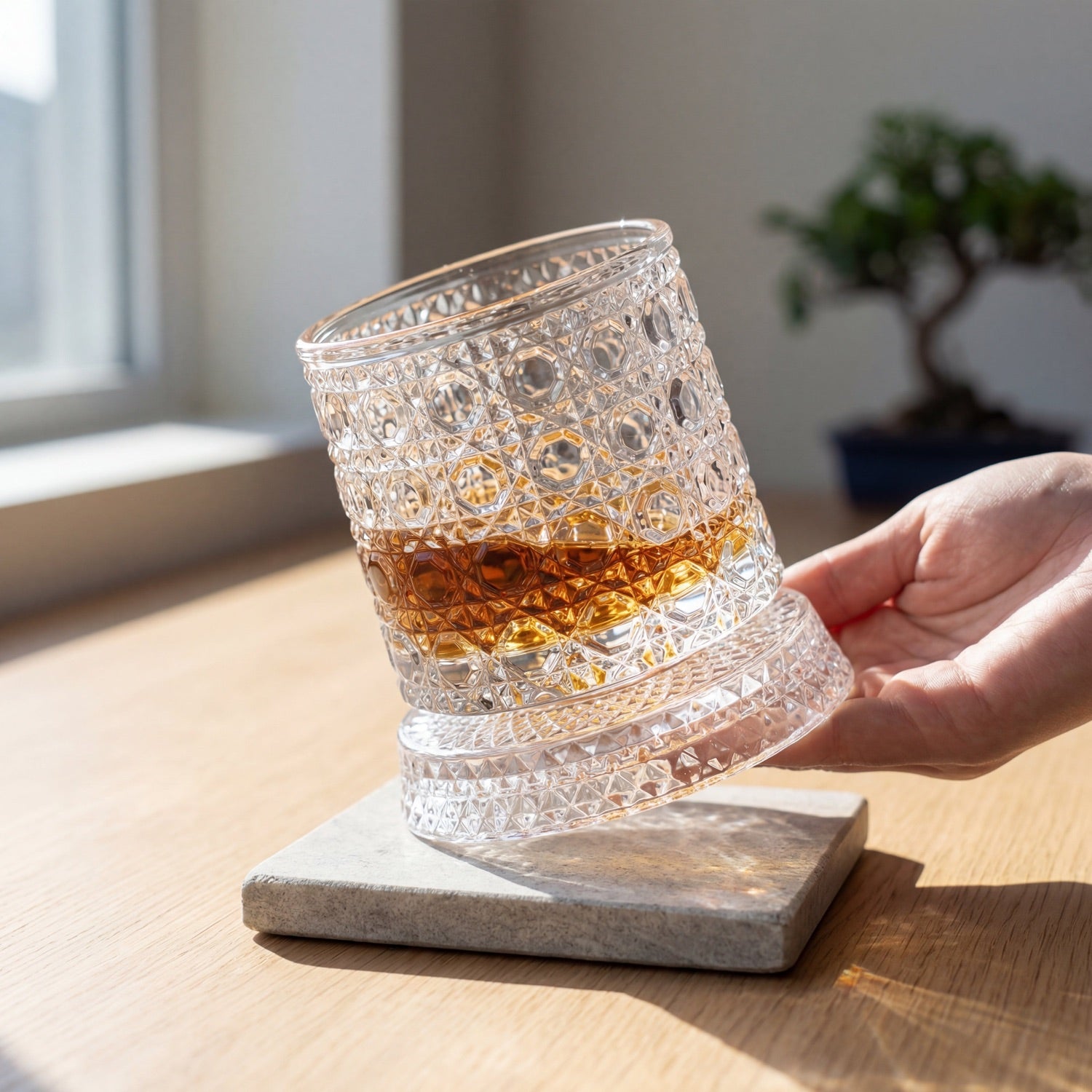 Hand hält drehendes Whiskyglas im warmen Licht